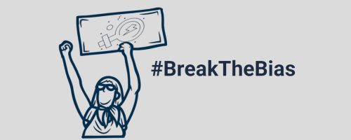 Das Bild zeigt eine Frau, die die Faust in die Luft reckt und in der anderen ein Protestplakat mit dem Weiblichkeitszeichen hält. Neben der Frau steht der Hashtag: Break the Bias.