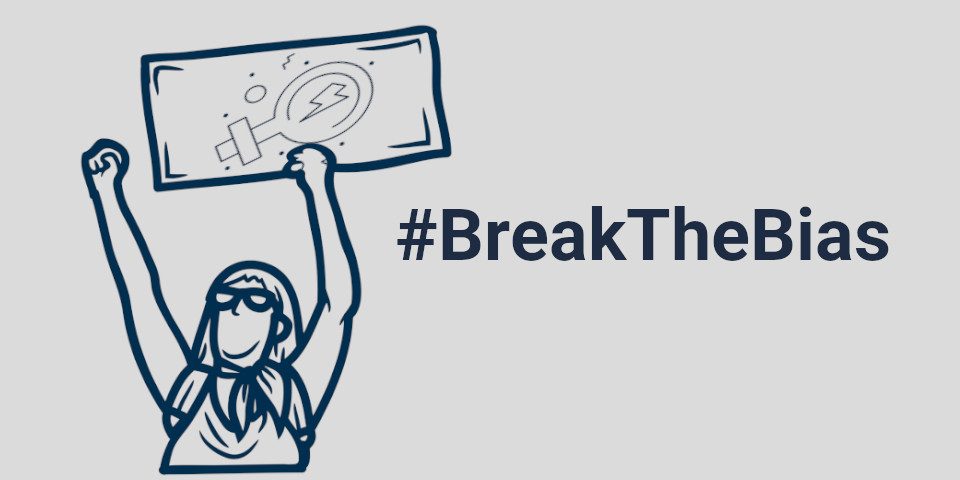 Das Bild zeigt eine Frau, die die Faust in die Luft reckt und in der anderen ein Protestplakat mit dem Weiblichkeitszeichen hält. Neben der Frau steht der Hashtag: Break the Bias.
