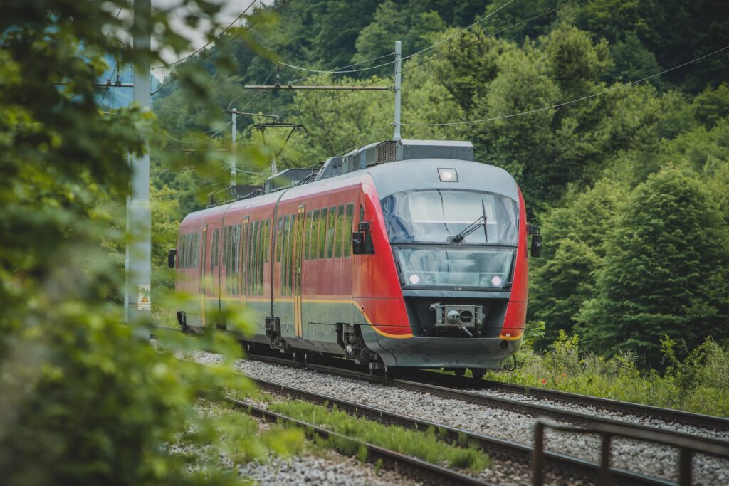 Das Bild zeigt einen roten Zug, der auf Schienen durch einen Wald fährt.