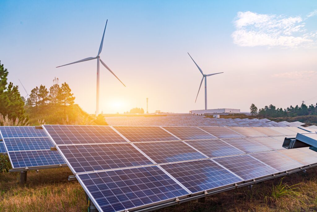 Das Foto zeigt Solarmodule auf einem Feld, im Hintergrund sind Windkrafträder zu sehen.