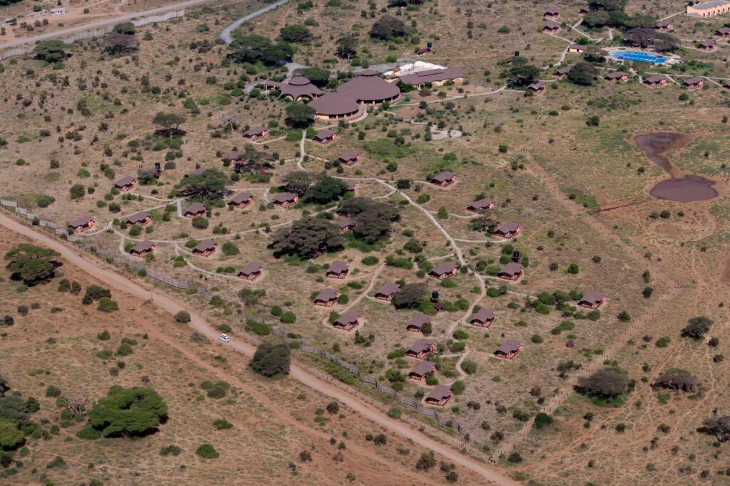 Das Foto zeigt eine Luftaufnahme von Kenia. Es sind runde Häuser und vereinzelte Büsche auf brauner Erde zu sehen.