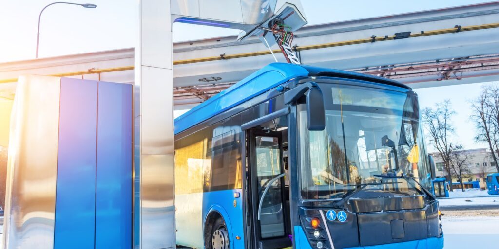 Das Foto zeigt einen blauen Elektro-Bus, der an einer Station geladen wird.