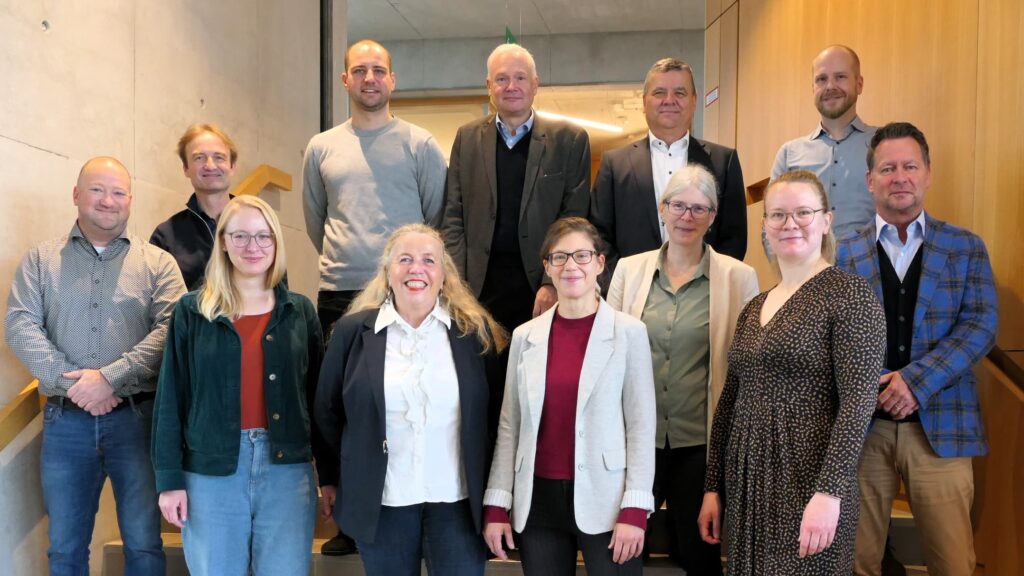 das bild zeigt eine gruppe von menschen, die auf einer treppe in zwei reihen augestellt sind, sie lächeln in die kamera