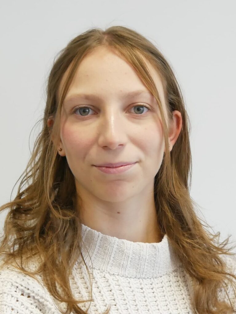 Das Bild zeigt eine junge Frau mit blonden langen Haaren, die freundlich in die Kamera guckt.