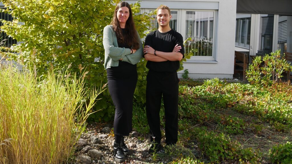 Das Foto zeigt zwei Personen in einem Garten, eine Frau, links und einen Mann, rechts, die beide freundlich in die Kamera blicken.