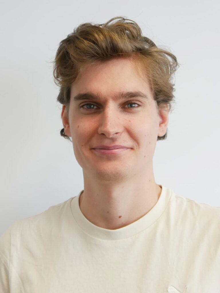 DAs Bild zeigt einen jungen Mann mit kurzen blonden Haaren, der in die Kamera blickt.